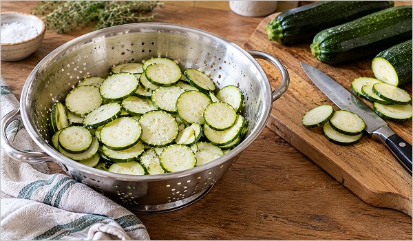 Rondelles de courgettes salées qui dégorgent dans une passoire avant la tarte